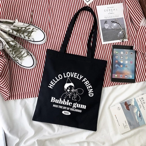 Flat lay of black canvas tote bag featuring bubble blowing cartoon print and casual props