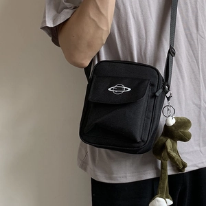 Close-up of black canvas crossbody bag with planet print and green frog plush charm