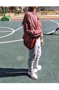 Detailed view of a red canvas crossbody bag styled with a plaid shirt and casual jeans