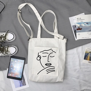Détail du sac cabas en toile blanche avec dessin visage minimaliste et bandoulière
