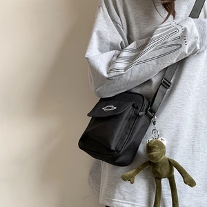 Close-up of a black canvas crossbody bag with planet logo and green frog plush pendant