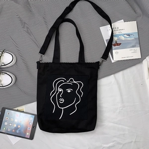 Détail du sac cabas en toile noire avec visage minimaliste et bandoulière amovible