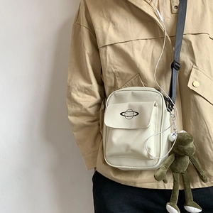 Detail of canvas crossbody bag with planet logo and green frog plush keychain accessory