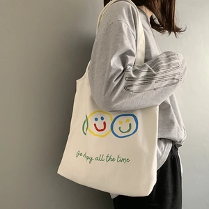 Detail of off-white canvas tote bag featuring colorful smiling faces and cursive text