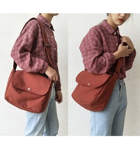 Detail of red-brown canvas crossbody envelope bag with silver buckle and adjustable strap