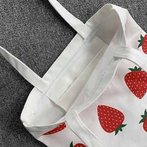 Close-up of strawberry print canvas tote bag showing zipper closure and inner pocket