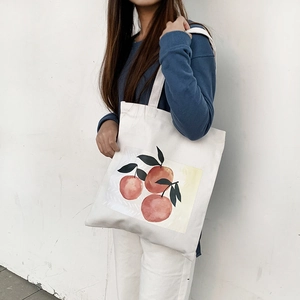Close-up of summer canvas tote bag with orange print worn on shoulder over white wall