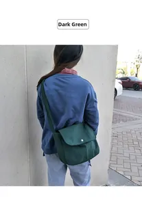 Dark green canvas messenger bag worn by a model showing size and drape in outdoor setting