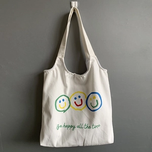 Detail of white canvas tote bag featuring three colorful smiley faces and happy quote