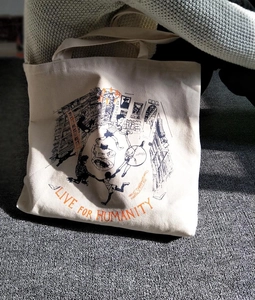 Off-white canvas tote bag featuring black artistic figure illustration and orange lettering