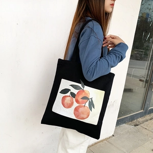 Minimalist black canvas tote bag with watercolor orange print worn on shoulder