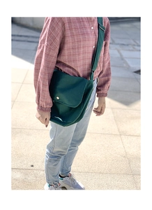 Outdoor shot of a model wearing a dark green canvas crossbody bag with metal buckle