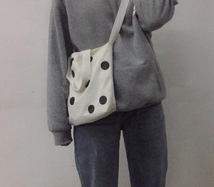 On-body view of a white canvas crossbody bag featuring large black polka dots