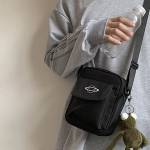 Close-up of black canvas crossbody bag with planet print and green frog plush charm