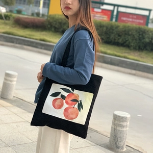 Detail of black canvas tote bag with watercolor orange print worn by a model in casual style