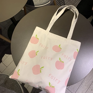 Detail of white canvas tote bag with pink peach prints and fairy lettering on table
