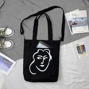 Détail du cabas en toile noire avec dessin au trait artistique et bandoulière réglable