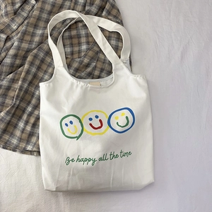 Detail of white canvas tote bag featuring colorful smiley faces and Be happy text print