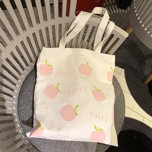Cute white canvas tote bag featuring pink peach prints and fairy lettering on a chair