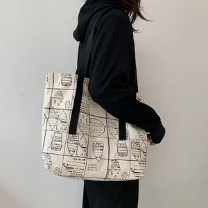 Detail of beige canvas tote with black graphic prints shown on a model's shoulder