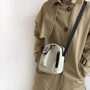 Detail of off-white canvas crossbody bag with black contrast strap on khaki trench coat