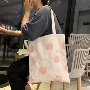 Close-up of white canvas tote bag with pink peach prints worn by a model in a cafe