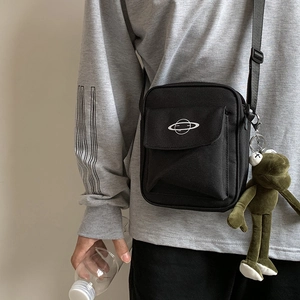 Detail of black canvas crossbody bag with planet print and green plush frog charm