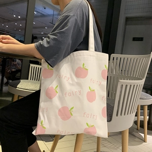 Close-up of a white canvas tote bag with pink peach prints and 'fairy' text detail