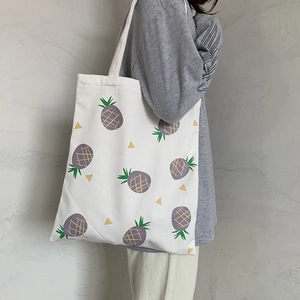 Détail d'un sac cabas en toile blanche avec imprimé ananas violet porté par un mannequin