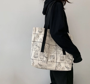 Close-up of a cream canvas tote bag featuring black artistic prints and wide shoulder straps