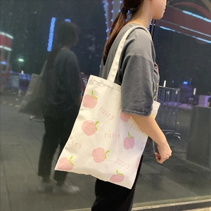 Close-up of white canvas tote bag featuring pink peach patterns and fairy text