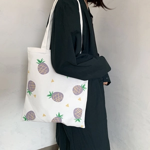 Détail du sac fourre-tout en toile blanche avec motif d'ananas violet et large bandoulière