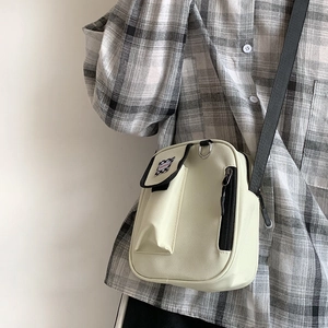 Detail of beige canvas crossbody bag with checkerboard pocket and adjustable black strap