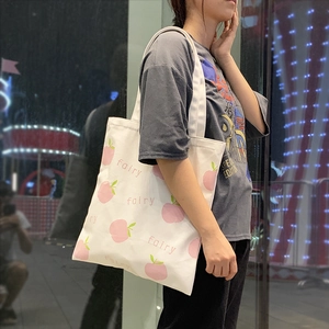 Detailed close-up of a white canvas tote bag with pink peach prints and fairy text