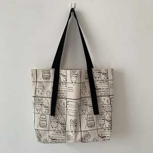 Detail of canvas tote bag with artistic black hand-drawn illustrations and black straps
