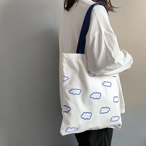 Détail d'un sac cabas en toile blanche avec motifs de nuages bleus porté par un modèle