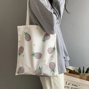 Gros plan d'un sac cabas en toile blanche avec motif ananas violet porté par un mannequin