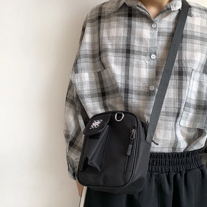 Black canvas messenger bag with fashion tag worn across the body by model in casual style
