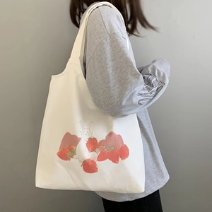 Détail du sac cabas en toile blanche avec imprimé lapin et fraise porté à l'épaule