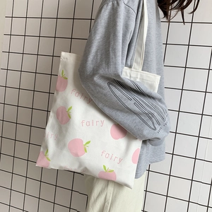 Detail of white canvas tote bag featuring pink peach print and fairy text lettering