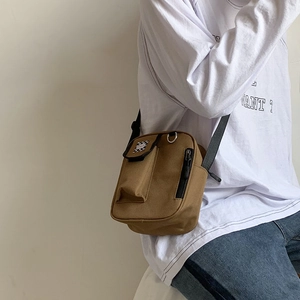 Detail of a brown canvas crossbody bag with a plaid front pocket and adjustable strap