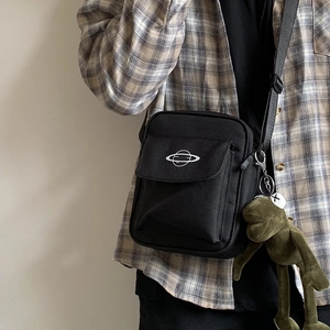 Black canvas crossbody bag with white planet embroidery and a green plush frog keychain