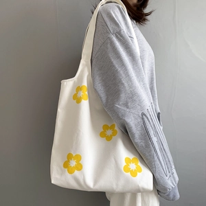 Close-up of white canvas tote bag with yellow floral print shown on model's shoulder