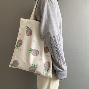 Détail du sac cabas en toile avec imprimé d'ananas violet et texture de tissu beige