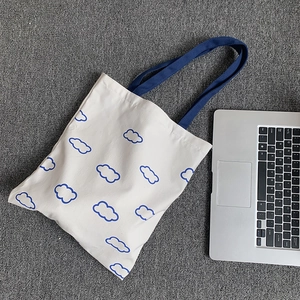 Vue détaillée d'un sac cabas en toile blanche avec motifs nuages bleus et anses longues