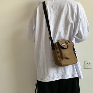 Detail of tan canvas crossbody bag with checkerboard pocket shown on a person