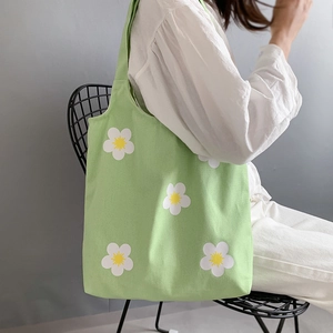 Green canvas tote bag with white daisy print shown in a lifestyle model setting