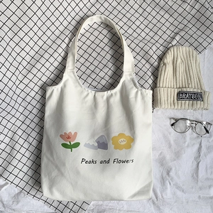Flat lay detail of a cream canvas tote bag featuring floral and peak artistic prints