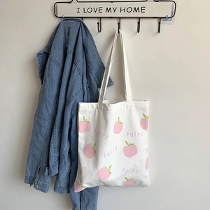 Close-up of white canvas tote bag featuring peach print and fairy text detail