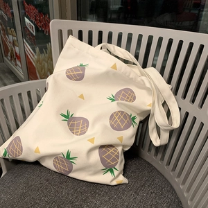 Détail du sac cabas en toile blanche avec imprimé ananas quadrillé violet sur une chaise